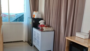 A room with a large window, a white cabinet with a microwave, and a wooden shelf. - Habor House by Koh Larn Riviera (Koh Lan)
