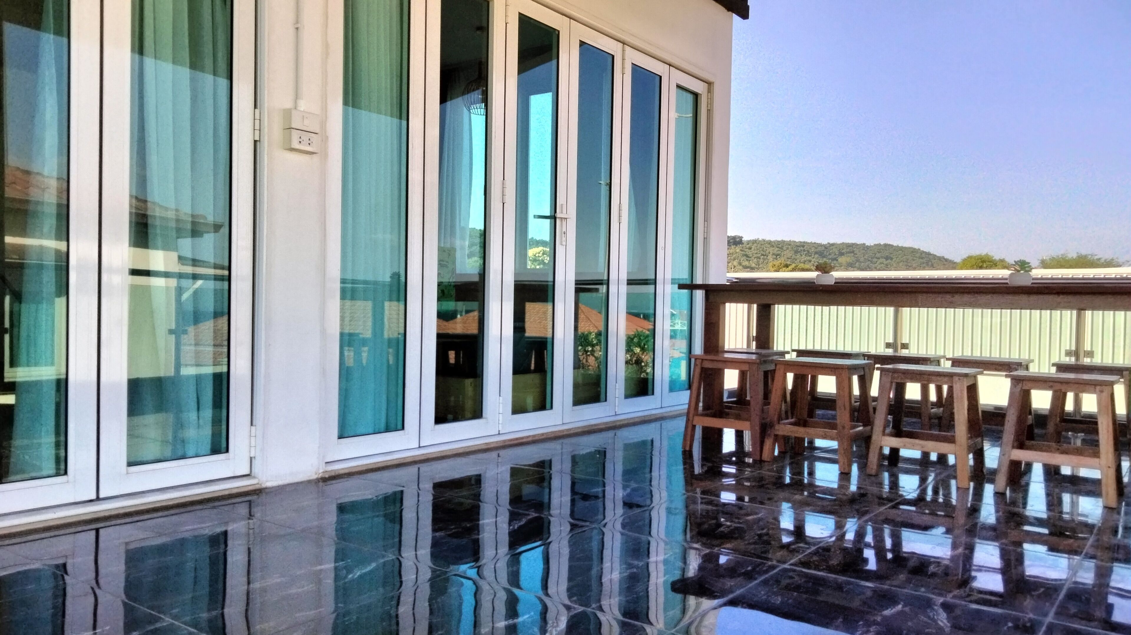 A modern building with large windows, a balcony with wooden furniture, and a reflective floor.
