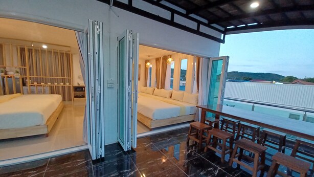 A modern hotel room with a large bed, a balcony with wooden furniture, and a view of the landscape. - Habor House by Koh Larn Riviera (Koh Lan)