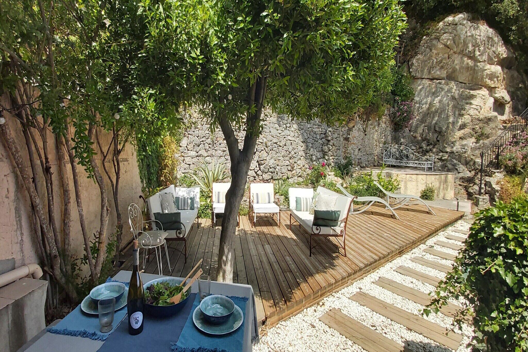 An outdoor dining area with a wooden deck, white chairs, and a table set for two.