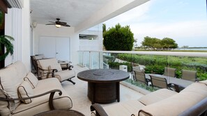 A balcony with outdoor seating, a ceiling fan, and a view of a landscaped area.