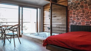 A room with a bed, a wooden floor, a stone wall, a glass door leading outside, and a small table with chairs. - Kulübem Etkinlik ve Konaklama (Ankara)