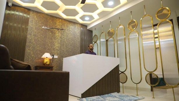 A reception area with a modern design, including a white reception desk, a patterned rug, and a ceiling with hexagonal lighting. - Hotel Lyf Suites - bahadurgarh (Bahadurgarh)