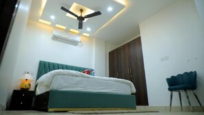 A bedroom with a bed, a ceiling fan, recessed lighting, an air conditioner, a wardrobe, and a chair. - Hotel Lyf Suites - bahadurgarh (Bahadurgarh)