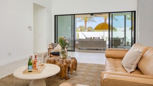 A modern living room with a leather sofa, a coffee table, and a dining area with a glass door leading outside.