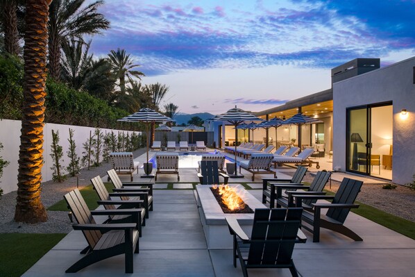 An outdoor lounge area with lounge chairs, a fire pit, and umbrellas.