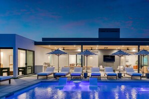 A modern outdoor pool area with lounge chairs and umbrellas, a covered seating area, and a clear view of the pool.