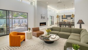 Una sala de estar moderna con sofá, sillón y mesa de centro. Se aprecia una chimenea y un comedor al fondo.