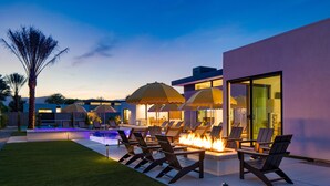 Un área de descanso al aire libre con piscina, fogata y sillones.