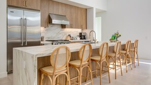 Una cocina moderna con una isla grande, refrigerador de acero inoxidable, armarios de madera y encimera de mármol.