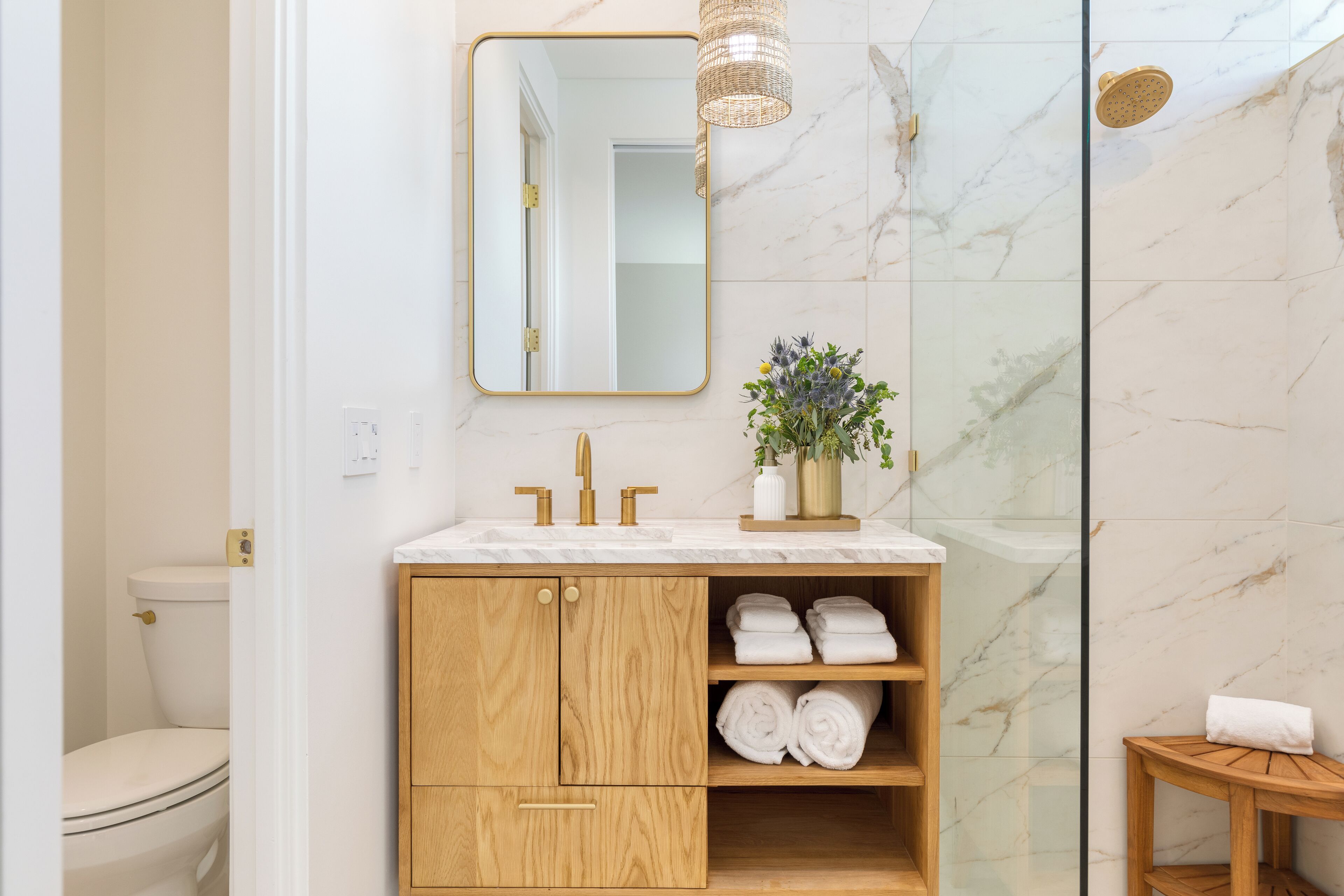Ein modernes Badezimmer mit einer Marmerdusche, einem Holzbadezimmermöbel mit goldenem Wasserhahn und einem Spiegel über dem Waschbecken.