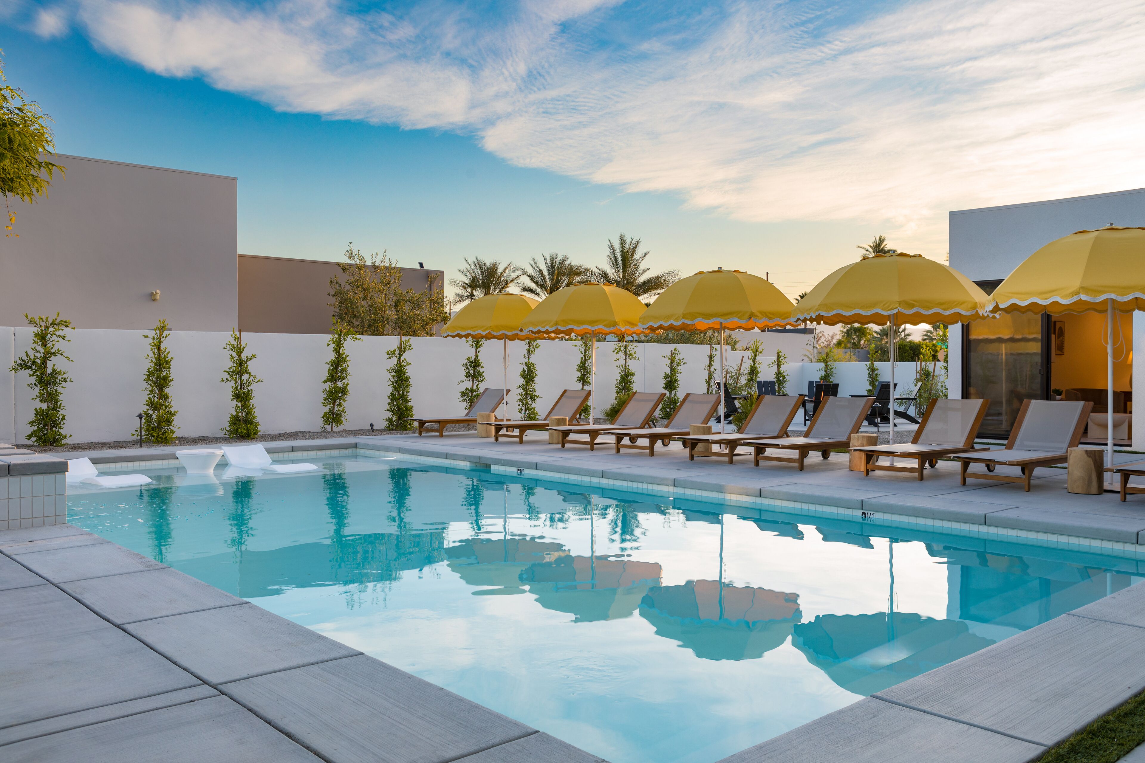 A swimming pool with lounge chairs and yellow umbrellas, surrounded by a low white wall and greenery.