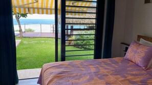 Une chambre avec un lit, une vue sur l’océan et un patio doté d’un toit de chaume.