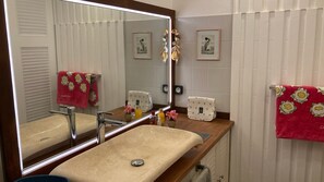 Une salle de bain avec un grand miroir, un lavabo, deux tableaux encadrés accrochés au mur et deux serviettes à motifs floraux.