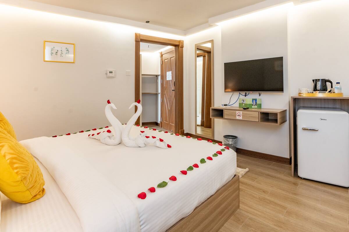 A hotel room with a bed, a TV, a minibar, and a door leading to a bathroom.