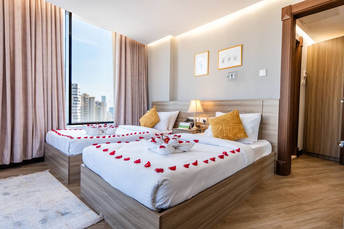 A hotel room with two beds, a large window, and a city view.