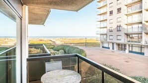 Varanda com mesa e cadeiras, com vista para área ajardinada e um edifício com várias varandas.