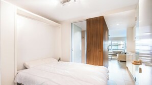 Quarto moderno com uma cama grande, um guarda-roupa de madeira e uma porta de vidro que dá para uma sala de estar.