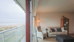 En balkon med udsigt til stranden, en sofa, en stol og en lampe.