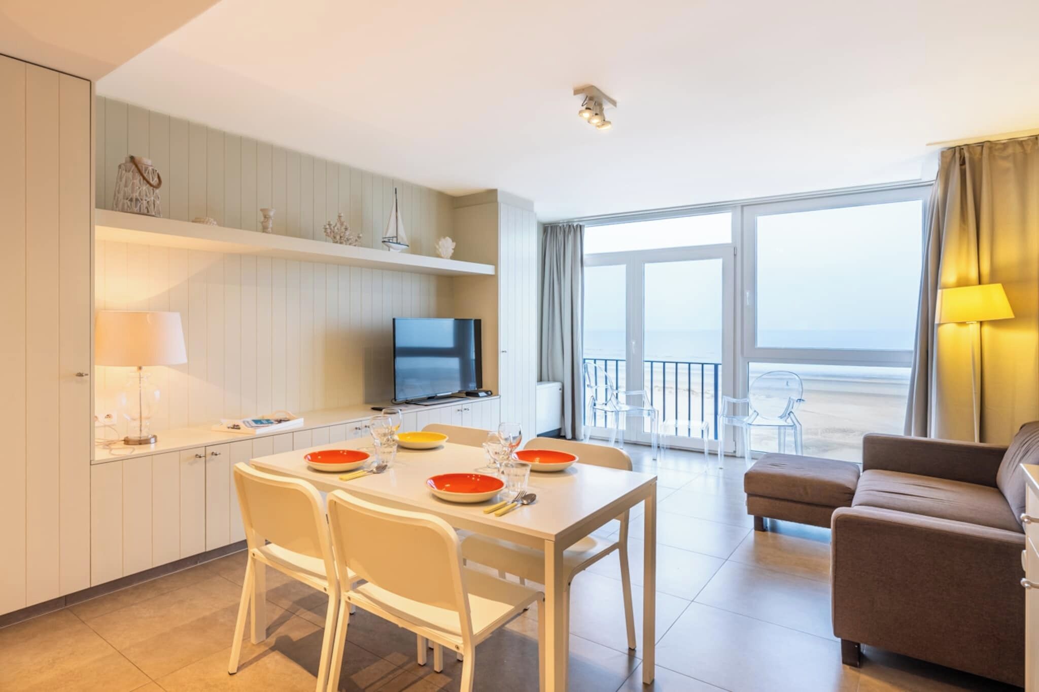 A modern hotel room with a dining area, a TV, a balcony with a view, and a sofa.