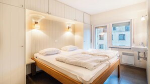 A modern bedroom with a wooden bed, built-in wardrobe, and a window with a view of a building. - Apartment by Belgian Coast with Beach Views (Oostduinkerke)