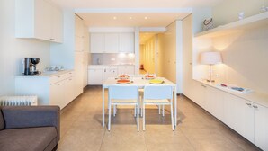 A modern kitchen with white cabinets, a dining table with chairs, and a sofa in the foreground. - Apartment by Belgian Coast with Beach Views (Oostduinkerke)