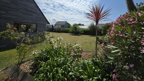 A modern house with a sloped roof, a well-maintained lawn, and various plants and flowers.
