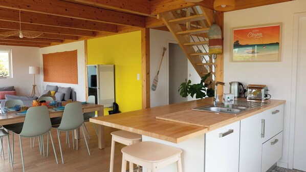 Una cocina moderna con una isla de madera, un comedor con sillas, una escalera y un cuadro en la pared.