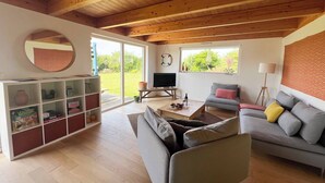A spacious living room with a wooden ceiling, a grey sofa, a television, and a bookshelf.