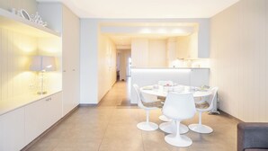 Une cuisine moderne avec des meubles blancs, un îlot central doté de sièges et un coin repas avec des chaises blanches.