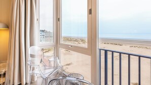 Une pièce dotée d’une grande fenêtre donnant sur une plage, ainsi que d’une chaise et d’une table.