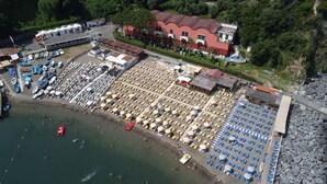 An aerial view of a beachside property with multiple beach umbrellas, lounge chairs, and a parking area. - Marea Luxury Rooms (Vico Equense)