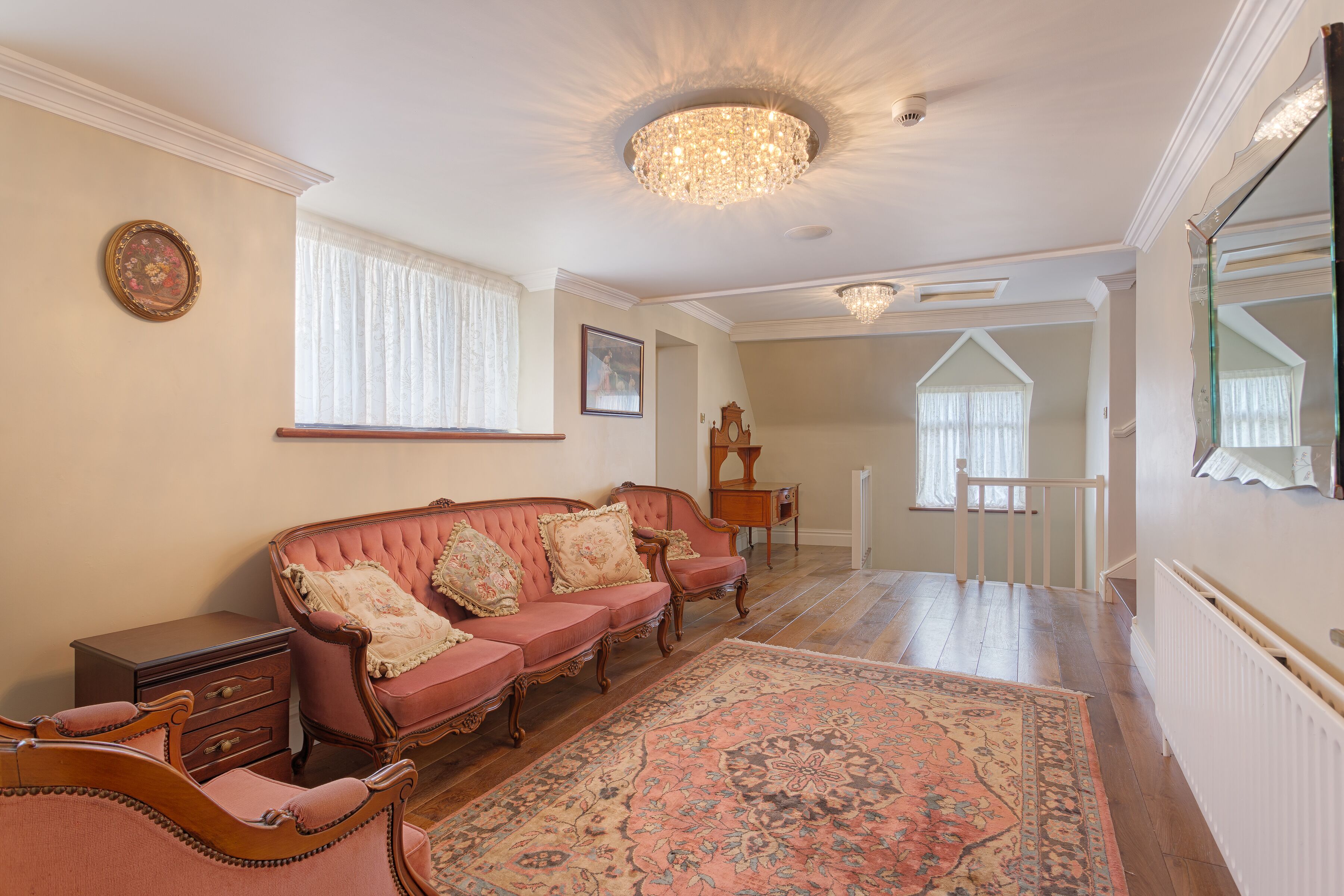 A spacious living room with a large pink sofa, a wooden coffee table, and a patterned rug.