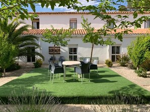 A patio with a round table and chairs, surrounded by a well-maintained lawn and a building with a tiled roof. - Ermita del Carmen  (Hijar)
