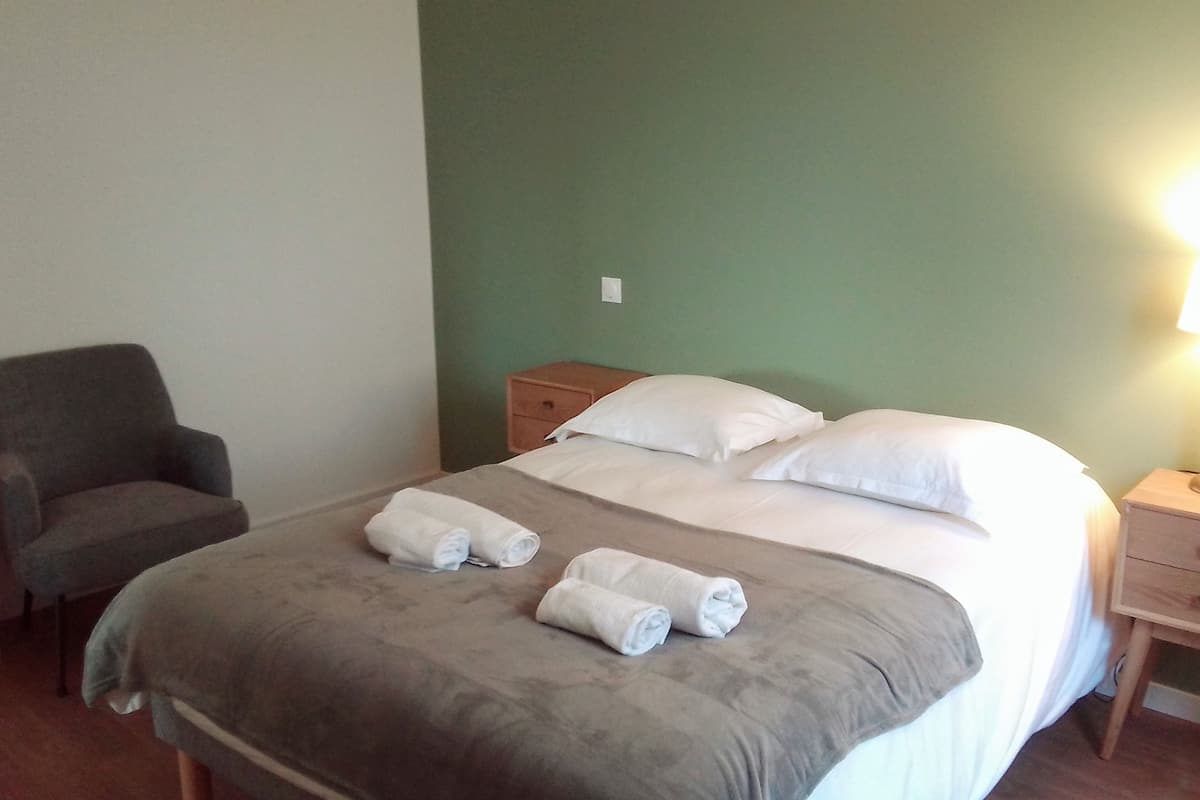 Une chambre d’hôtel avec un lit, deux tables de chevet, une chaise et un mur vert.