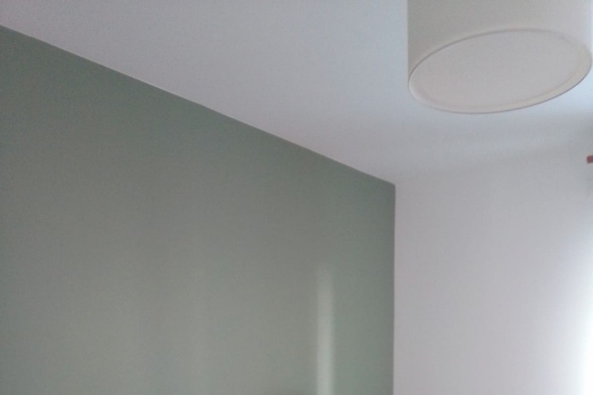 Un lit bien fait, avec des oreillers blancs et orange, un plaid jaune, une lampe de chevet et un radiateur.
