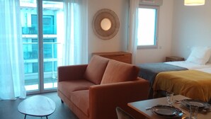 Une chambre d’hôtel moderne, équipée d’un canapé, d’une table à manger avec des chaises, d’un lit et d’une grande fenêtre avec des rideaux.
