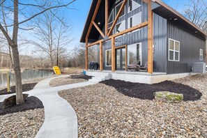 A modern house with a large deck, a pathway leading to the entrance, and a body of water in the background.