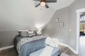 A bedroom with a bed, a ceiling fan, a nightstand, and a window.