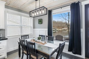 A dining area with a glass table, black chairs, a chandelier, and a view of a lake through large windows.