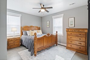 A bedroom with a wooden bed, nightstands, a dresser, and a ceiling fan.
