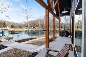 Un espacio al aire libre cubierto con vistas a un lago, terraza de madera y una parrilla.