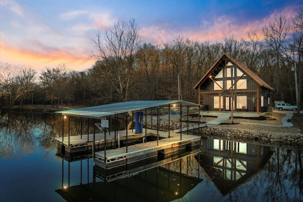 A lakeside cabin with a dock extending into the water, a covered deck, and a large windowed room.