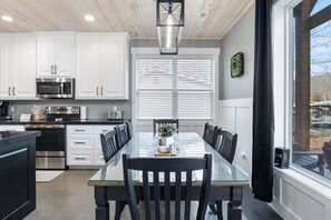 Una cocina moderna con armarios blancos, electrodomésticos de acero inoxidable y una mesa de comedor de vidrio con sillas.