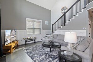 Ein Wohnzimmer mit grauem Sofa, Couchtisch, Bank und Treppe.