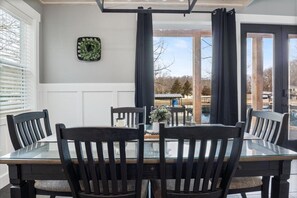 Un comedor con una mesa de vidrio y sillas negras, un adorno en la pared, y vistas al lago y árboles.