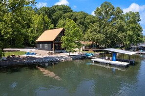 Una cabaña junto al lago con un muelle, rodeada de árboles y un cielo despejado.