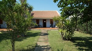 A house with a tiled roof, a paved pathway leading to the entrance, and a small patio with chairs and tables. - Villaggio le Palatine (Bernalda)