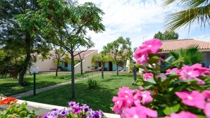A courtyard with a lawn, trees, and a building with a tiled roof. - Villaggio le Palatine (Bernalda)