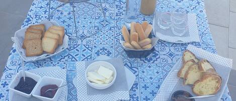 Une table dressée avec une variété d’aliments, notamment du pain, du fromage et des fruits, et ornée d’un motif décoratif en carreaux.